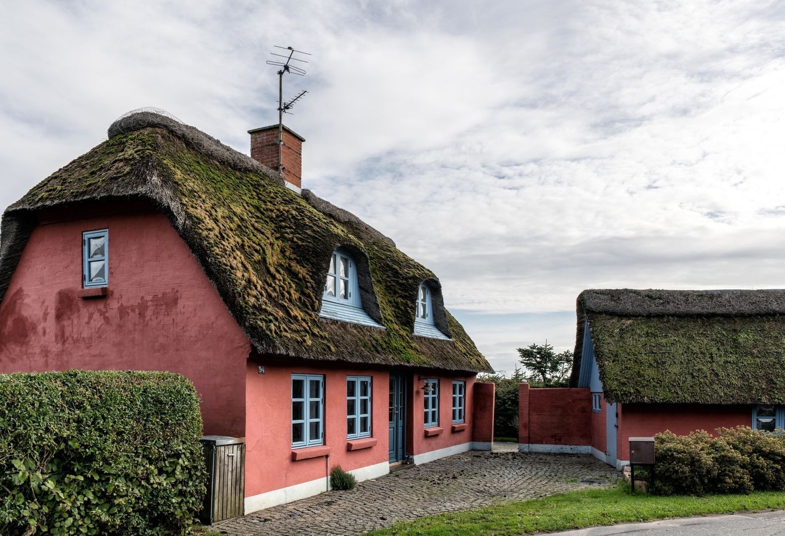 Røde, stråtækte historiske huse med mosgroede tage i en brostensgård