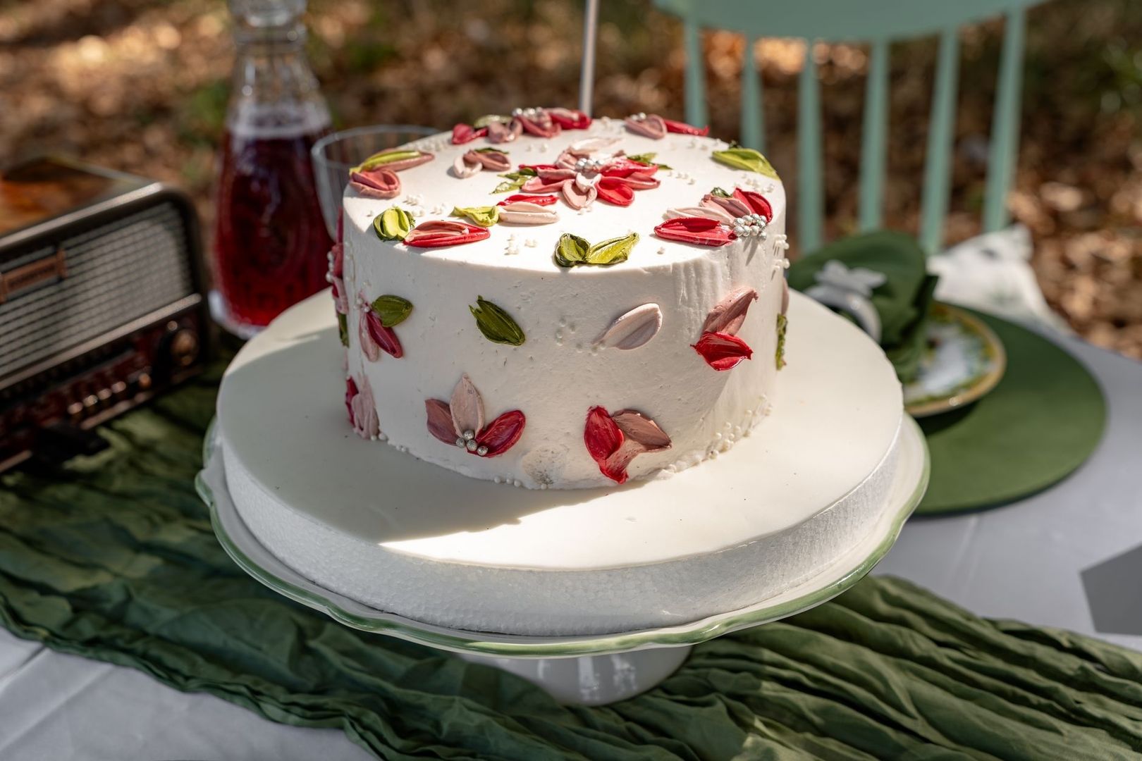 Hvid festkage pyntet med farverige blomster på et udendørs kaffebord